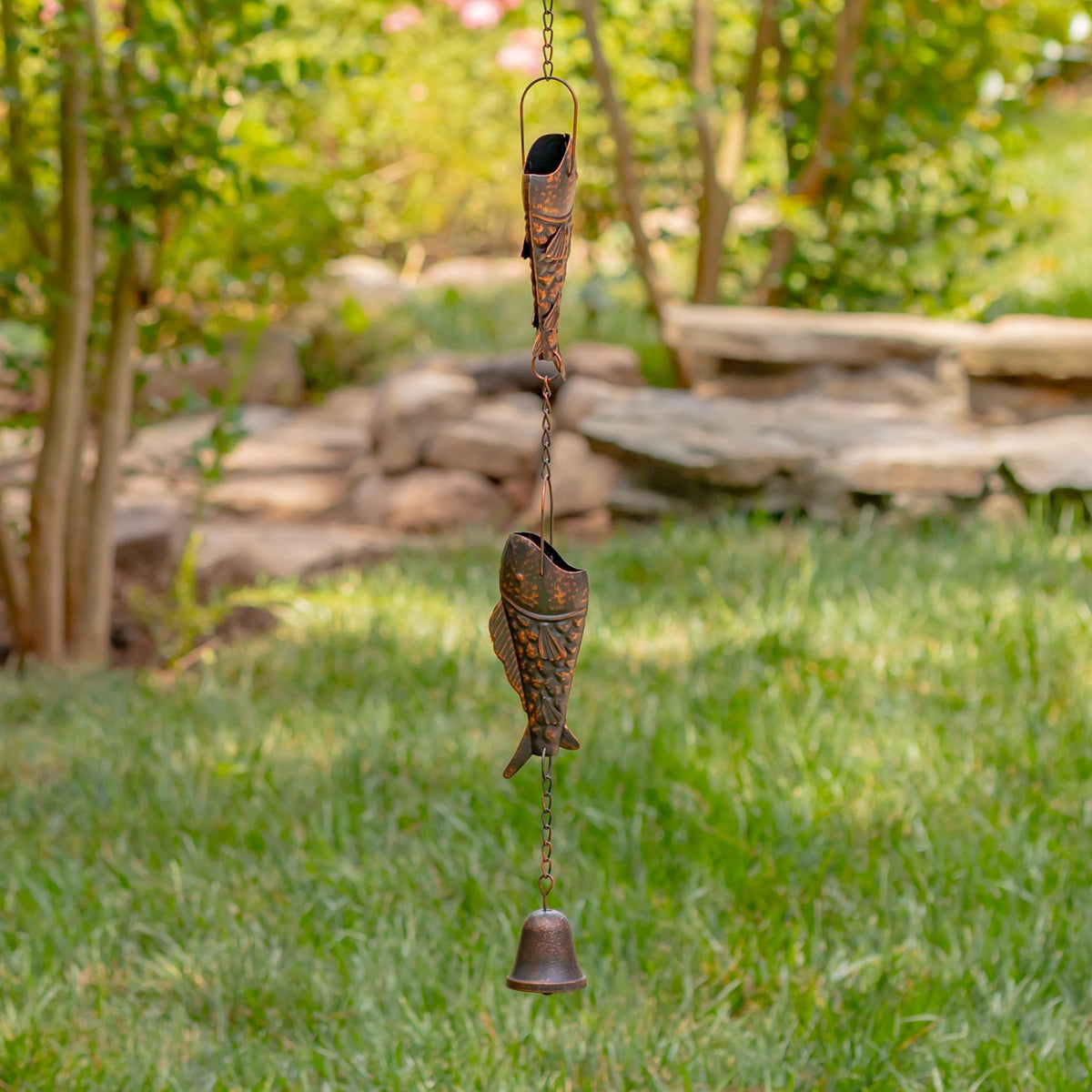 Antique bronze trout rain chain and bell hanging above a garden lawn