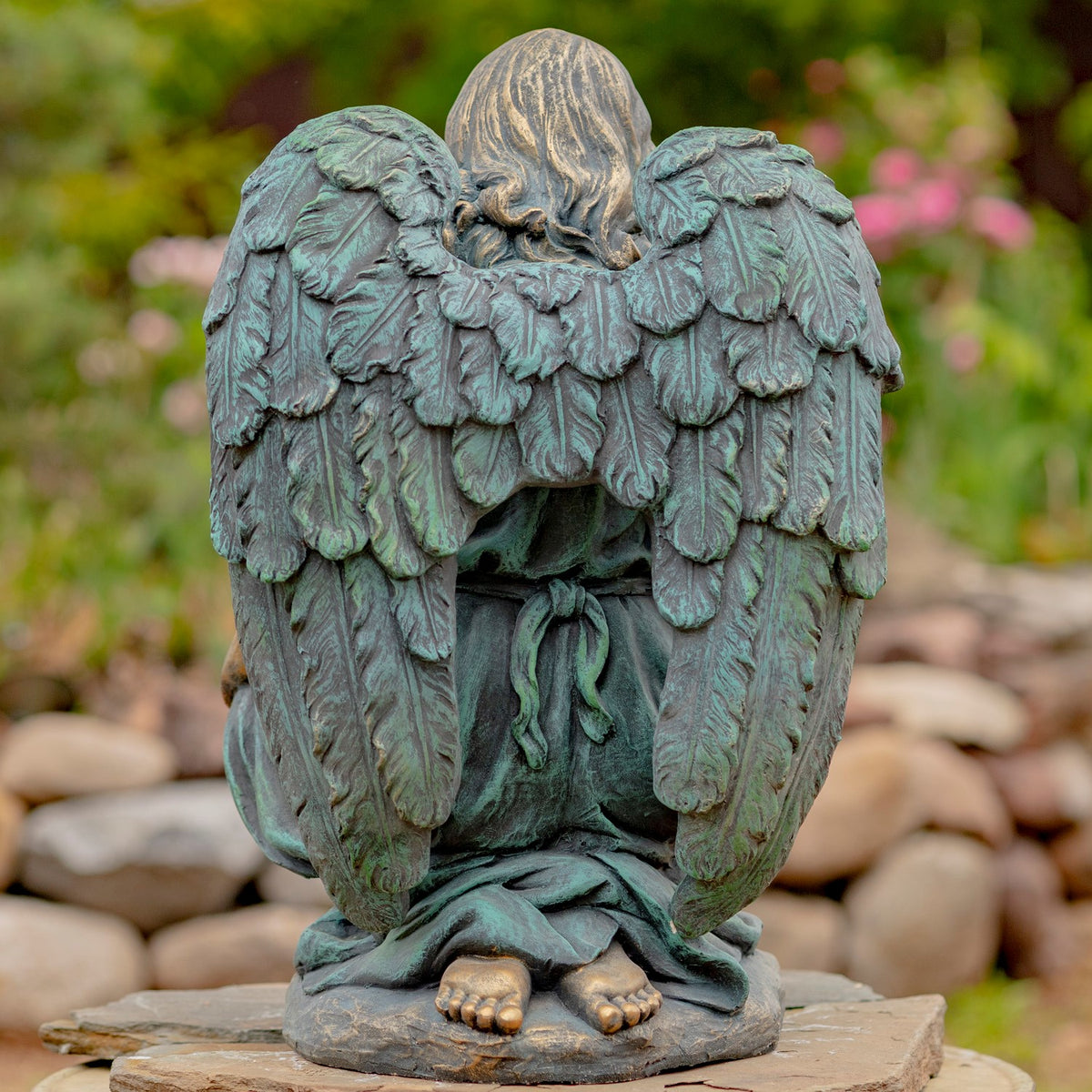 Rear view of the kneeling angel statue, showing layered wings, the back of its head, and bare feet.