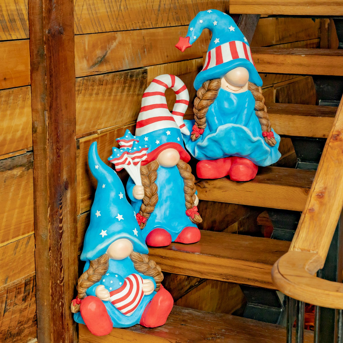 Three blue-and-red lady gnomes are arranged on wooden stairs.