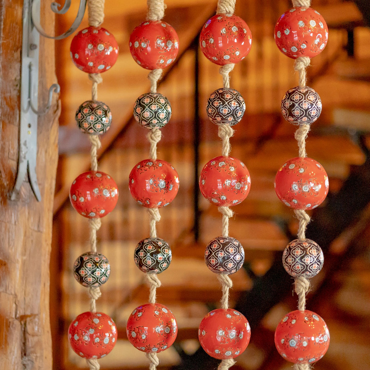 Four vertical strands show glossy red and dark patterned balls tied along thick natural-colored cords.