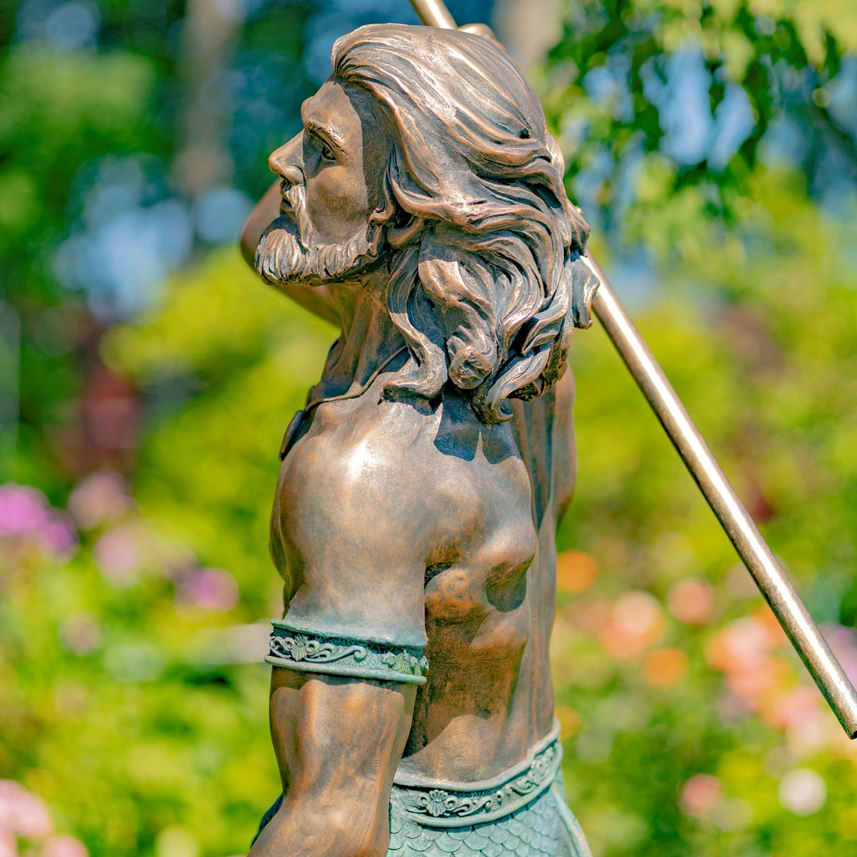 Side view of the merman statue’s upper body, long hair, patterned waist band, and diagonal trident shaft.