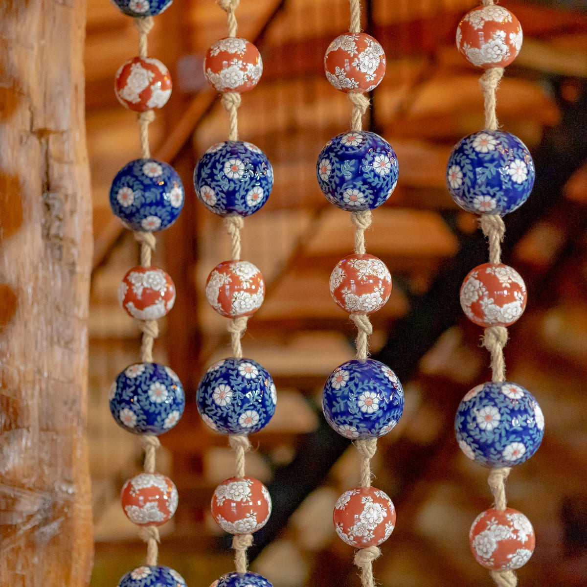 Several strands of blue and burnt-orange floral porcelain balls hang against a warm wooden background.