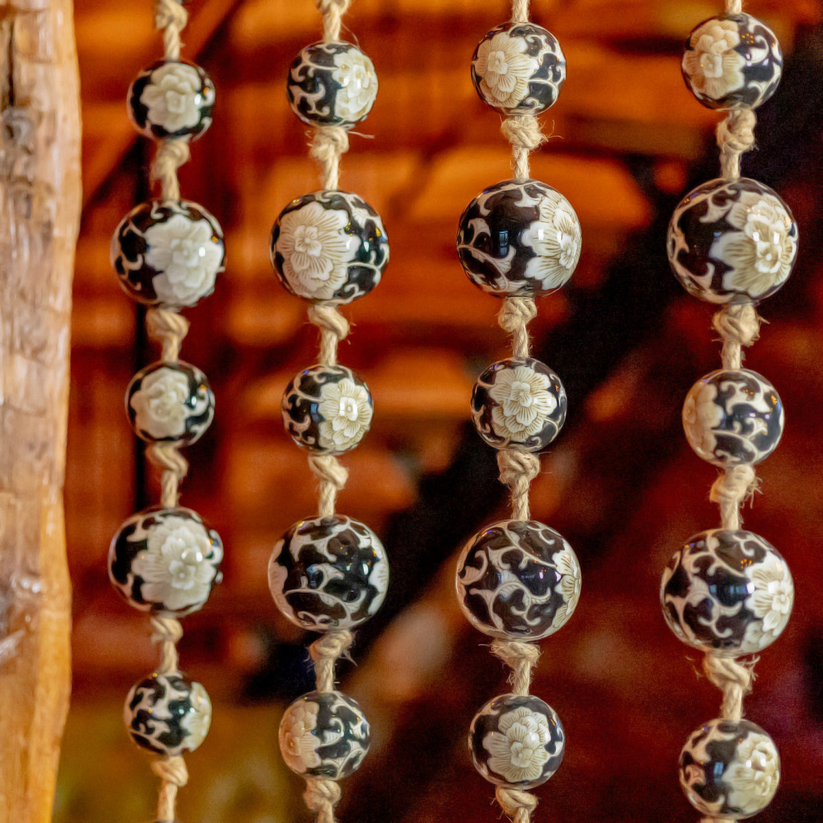 Several strands of glossy black-and-white balls with floral patterns hang against a blurred wood background.