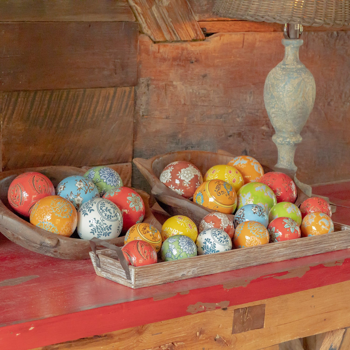 A wooden tray filled with colorful patterned ceramic balls rests on a red tabletop.