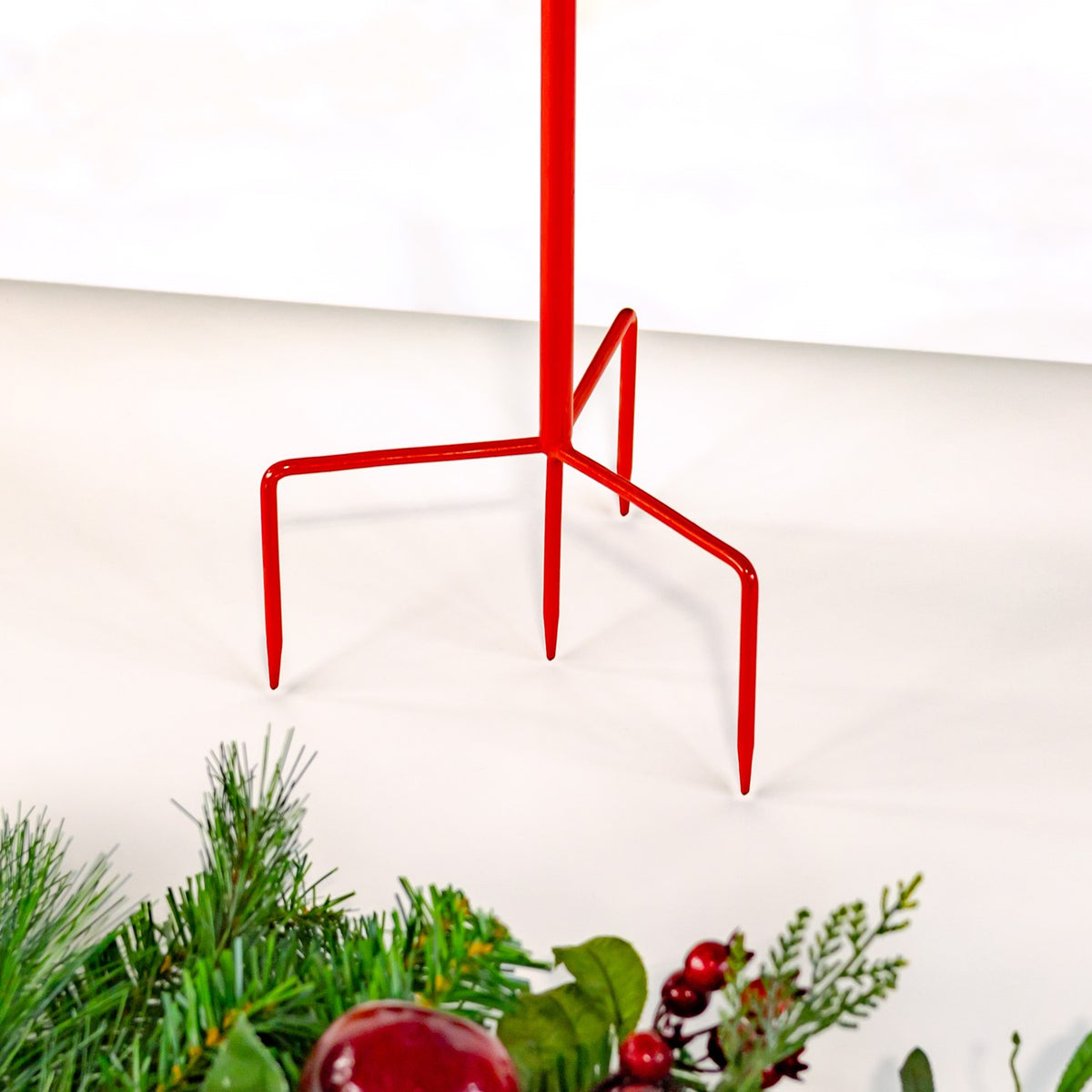 Red metal stake with three curved ground supports shown above evergreen branches.