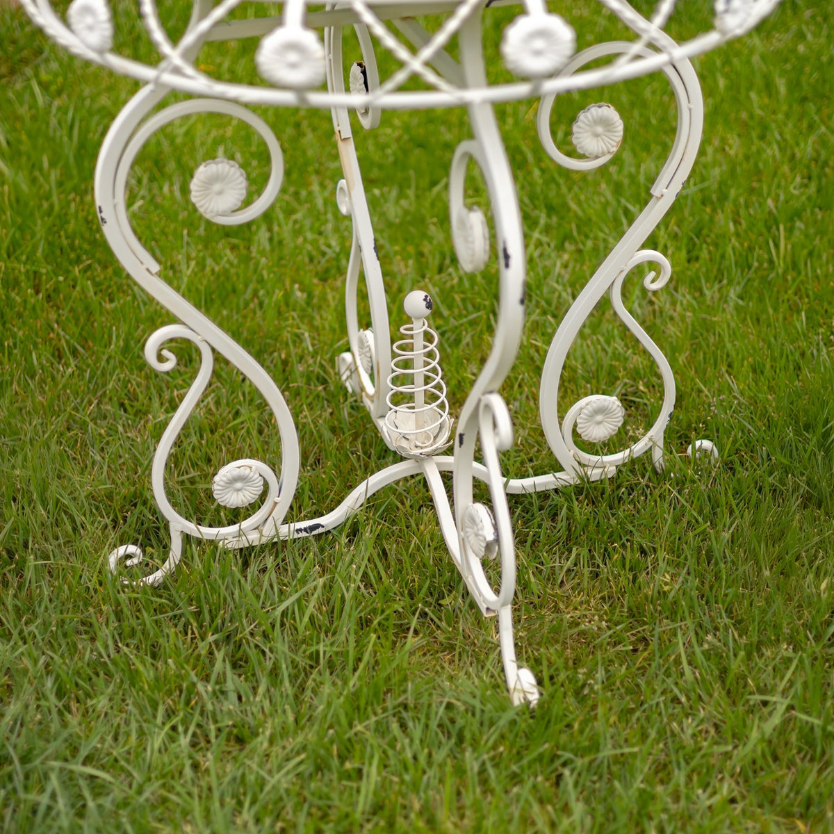 Curled metal legs and flower ornaments beneath the round table, shown against grass.