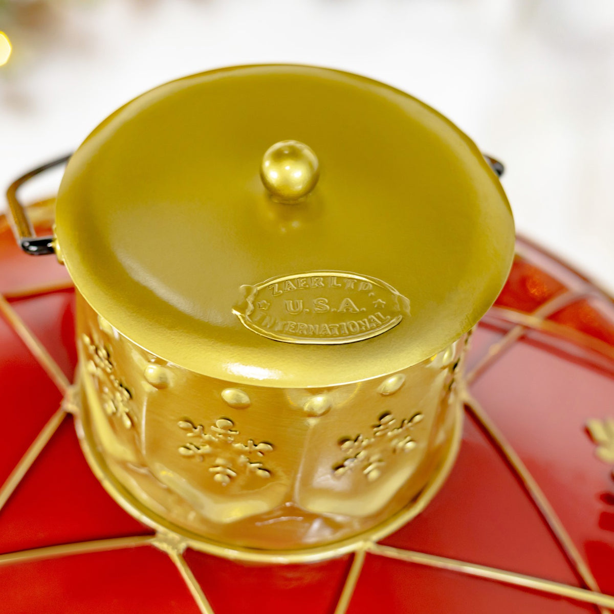 Gold-toned lid and raised top knob on the ornament, with its red body visible below.