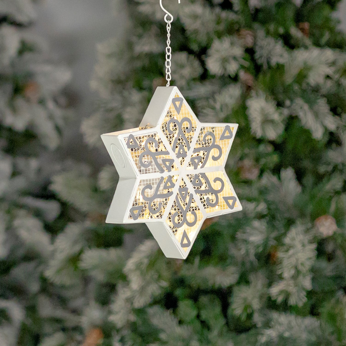 Single glowing white and silver six-point snowflake hanging against a softly blurred background