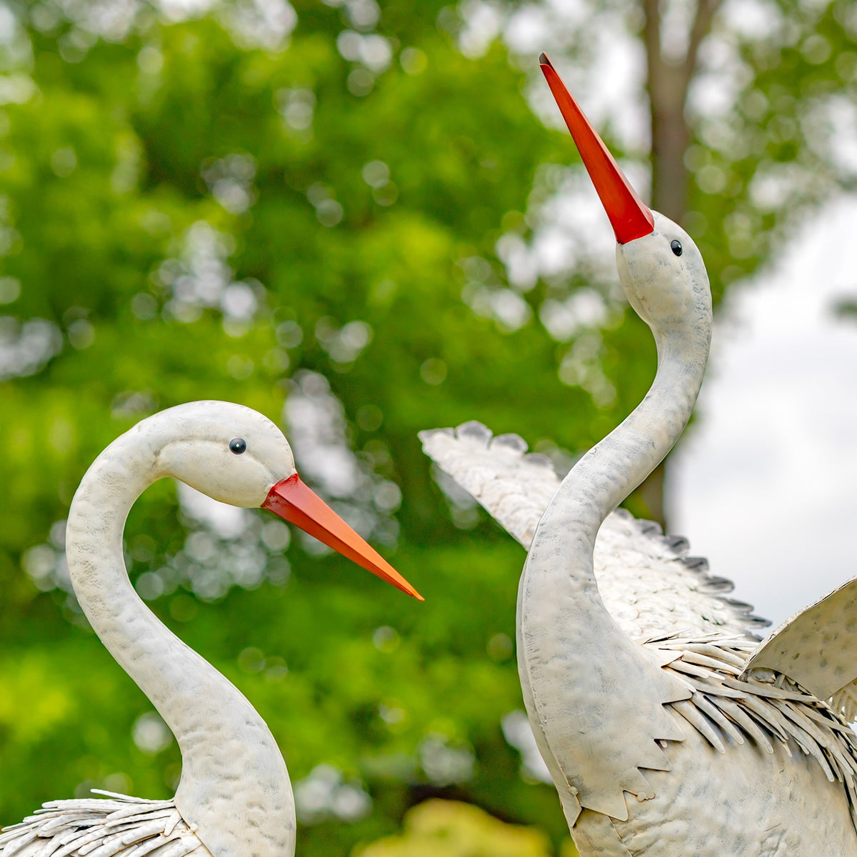 Close view of two heron figures showing their curved necks, orange beaks, and layered metal feathers.