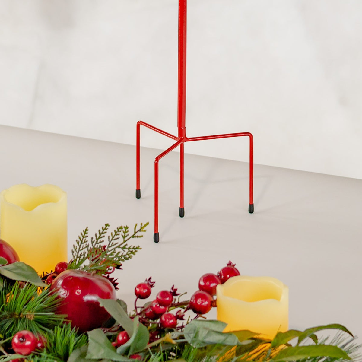 Red metal stake with a four-legged base and dark end caps beside candles and holiday greenery.