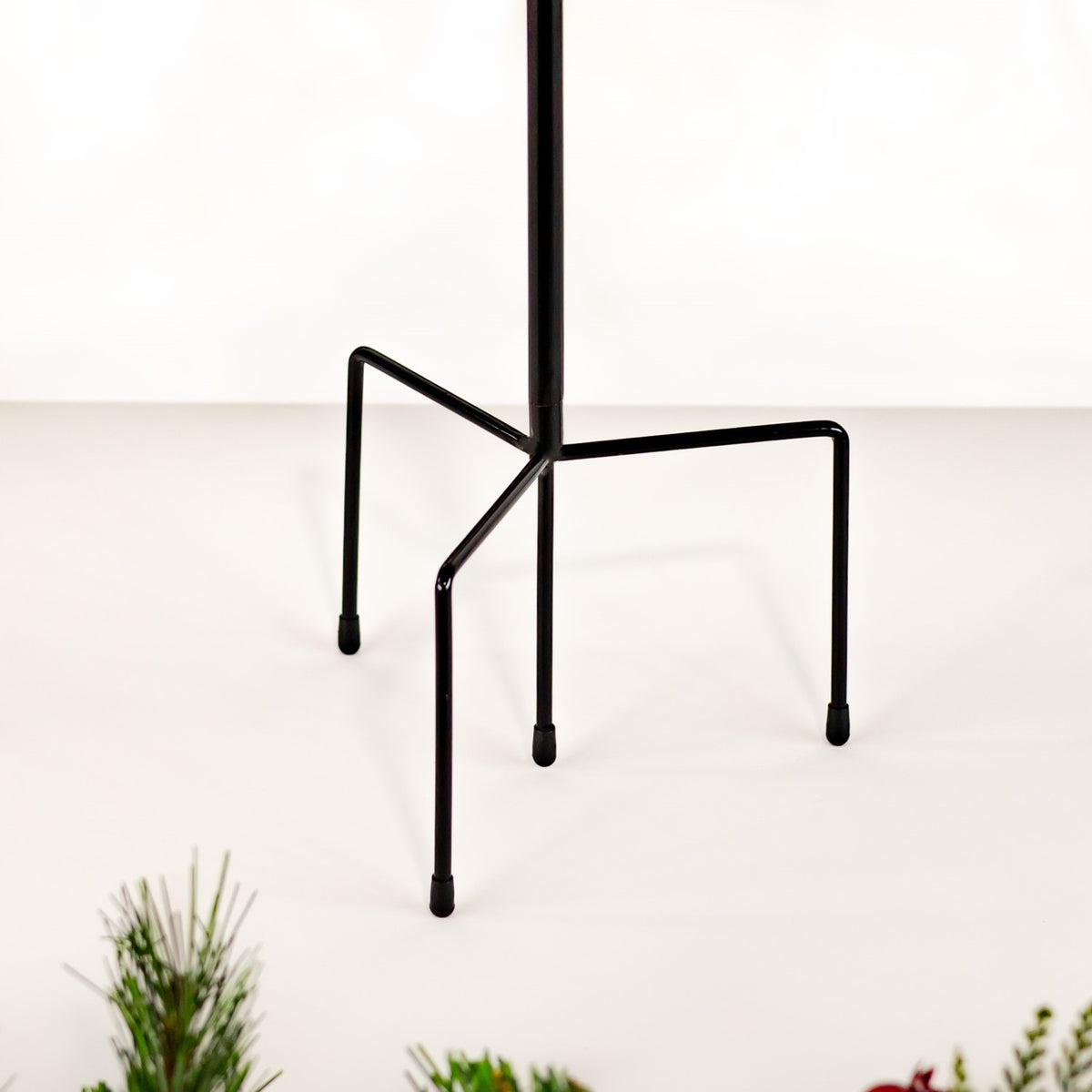 Black metal garden stake with a central pole and three splayed feet on a light background.