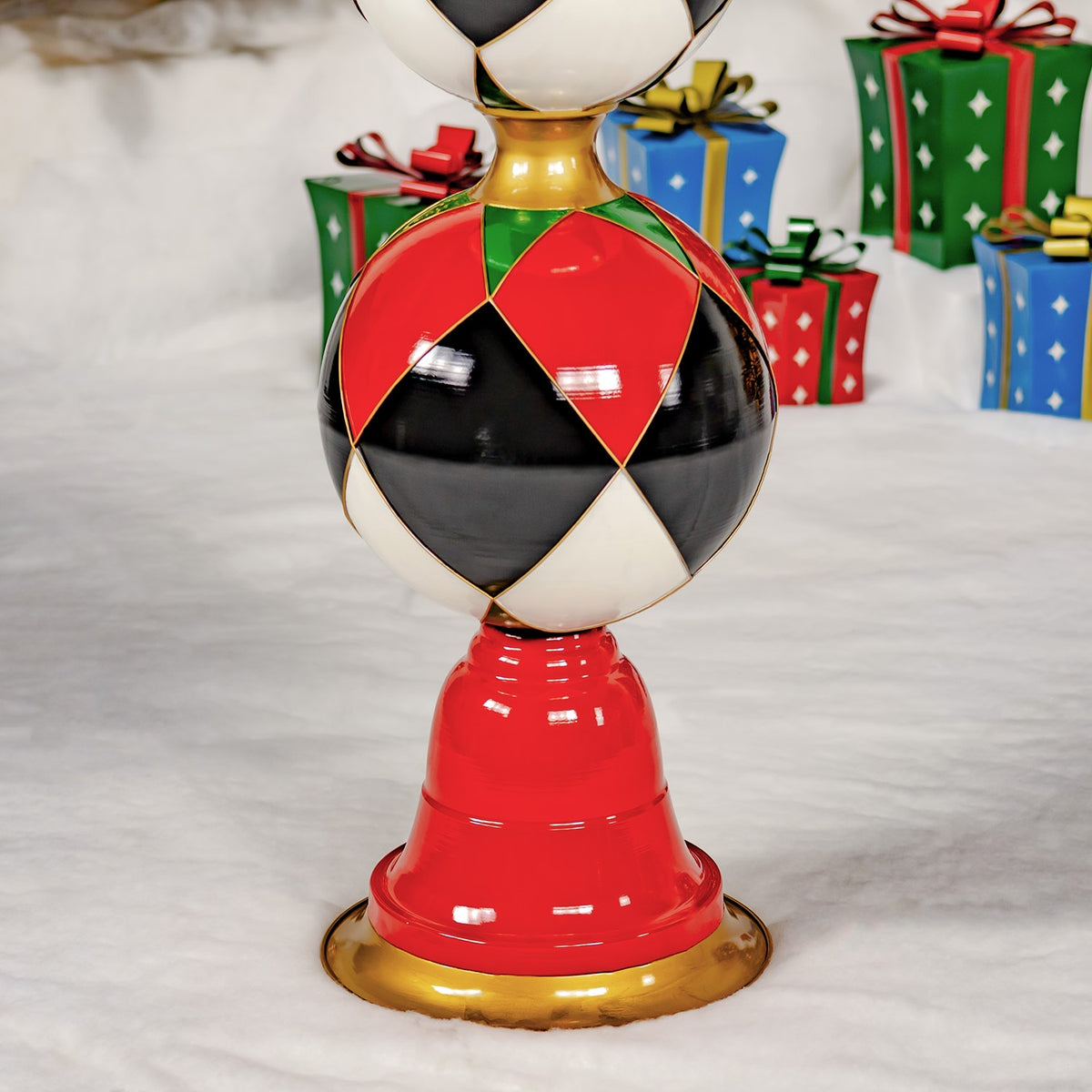 Close-up of the tower’s lower argyle-patterned ornament, red pedestal, and gold base with wrapped gifts behind it.