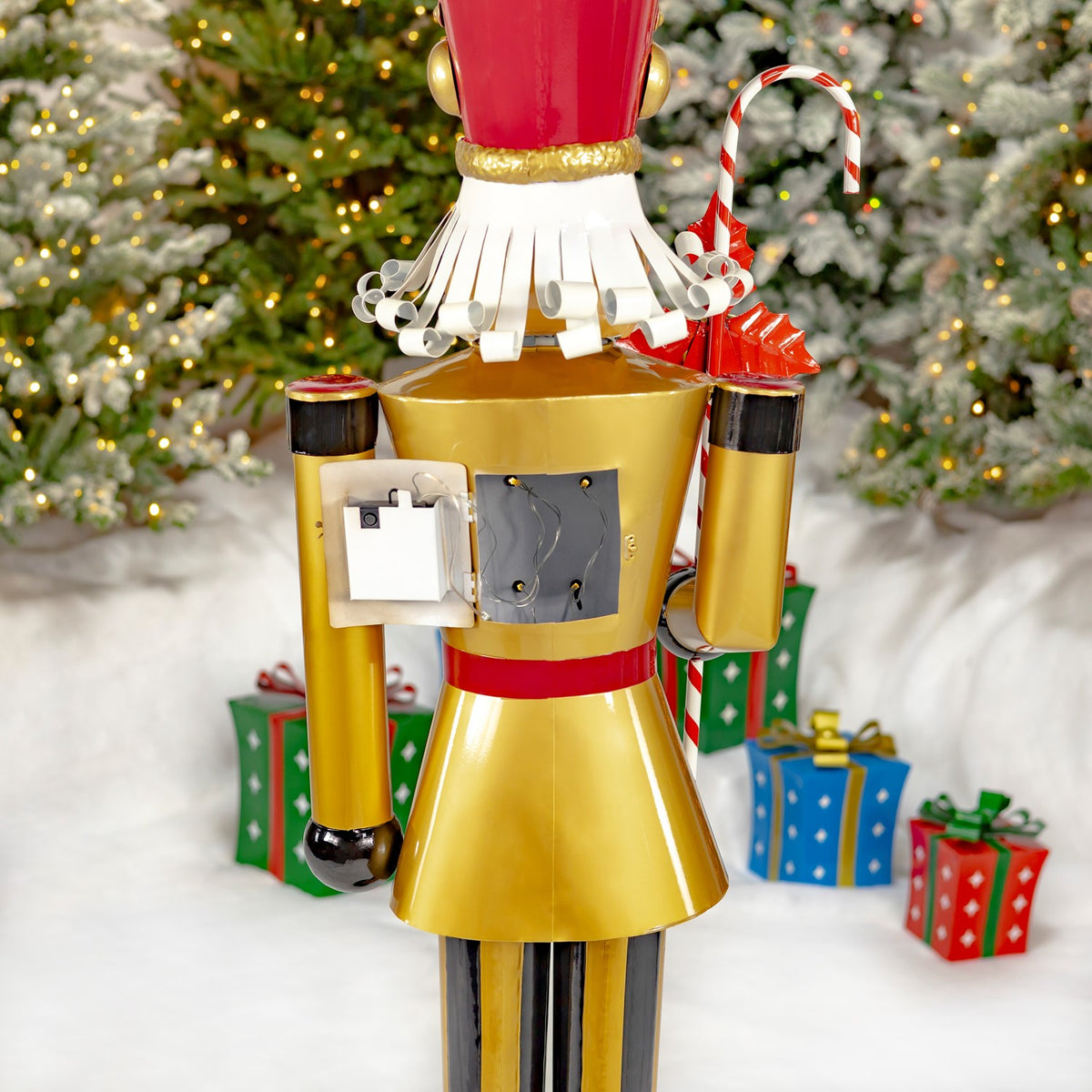 Rear view of the gold nutcracker showing its back panel, hanging candy cane, and red hat.