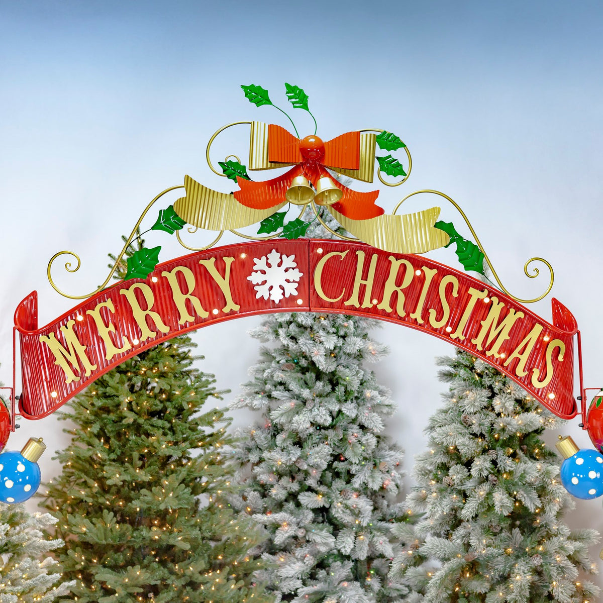 Curved red Merry Christmas banner with gold lettering above lit Christmas trees