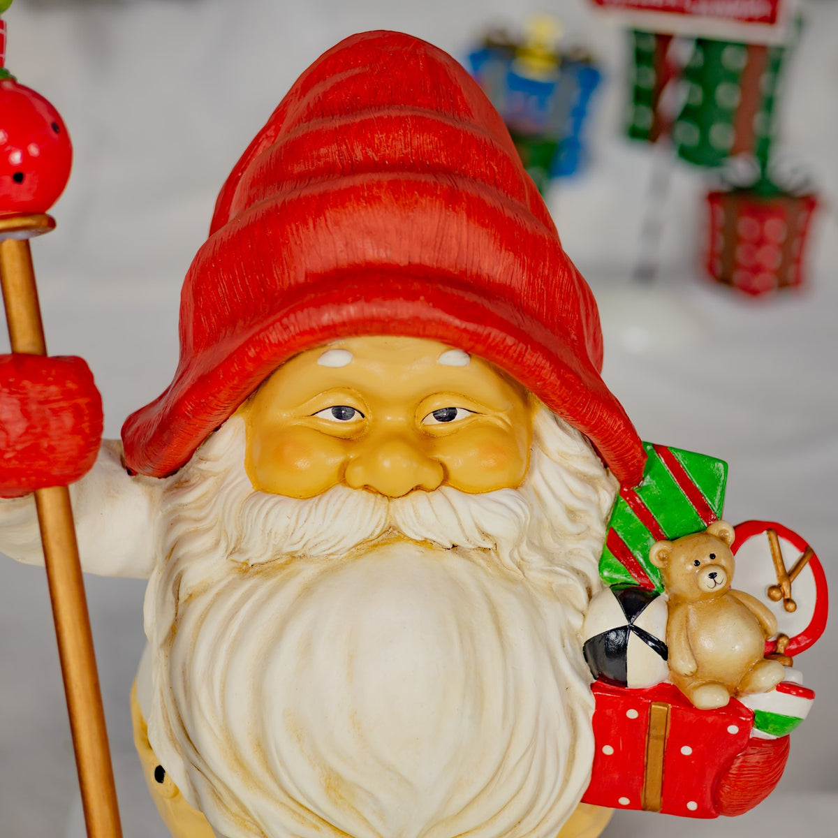 Close view of a gnome’s face, white beard and gift bundle with a small teddy bear.