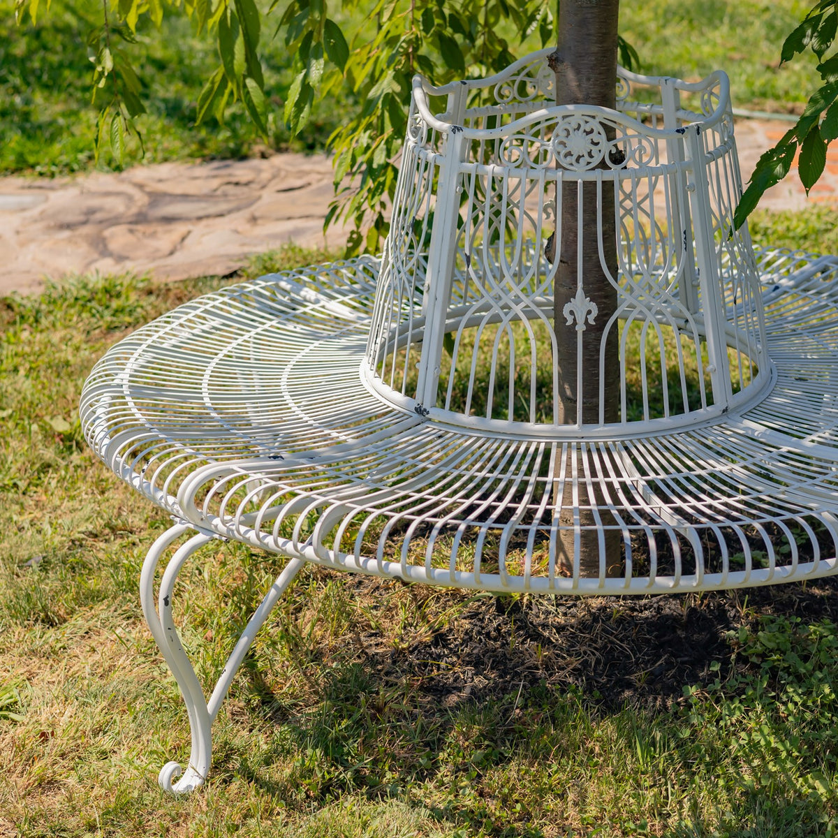 Round white metal bench arranged around a tree in a sunny garden.