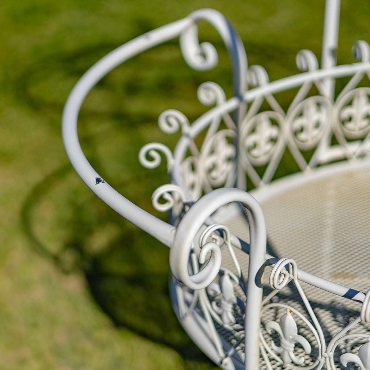Close-up of the cart’s curled white iron handle, scrollwork basket rail, and mesh base.