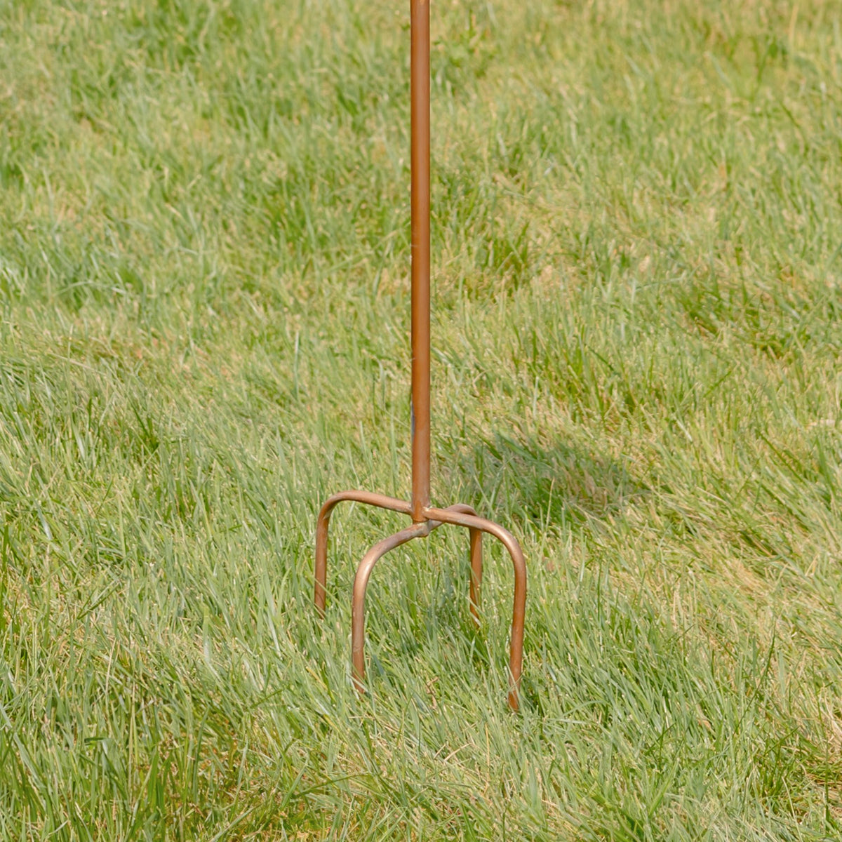 Long copper-colored stake ends in curved prongs planted in grass.