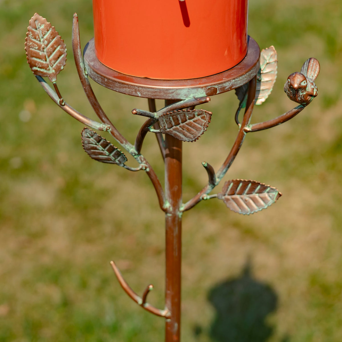 Metal branches with leaf ornaments and a small bird extend around the stake beneath the birdhouse