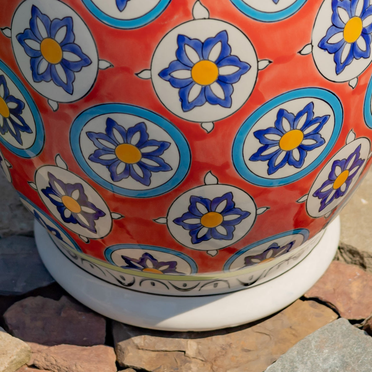 Lower side of the floral ceramic stool, showing its red patterned body, pale base band, and stone ground.