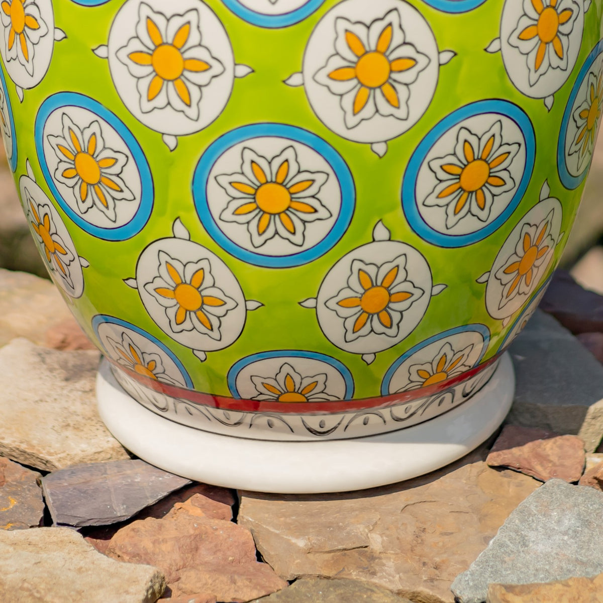 Lower portion of a green floral-patterned ceramic stool, showing its white base and decorative band on stone.