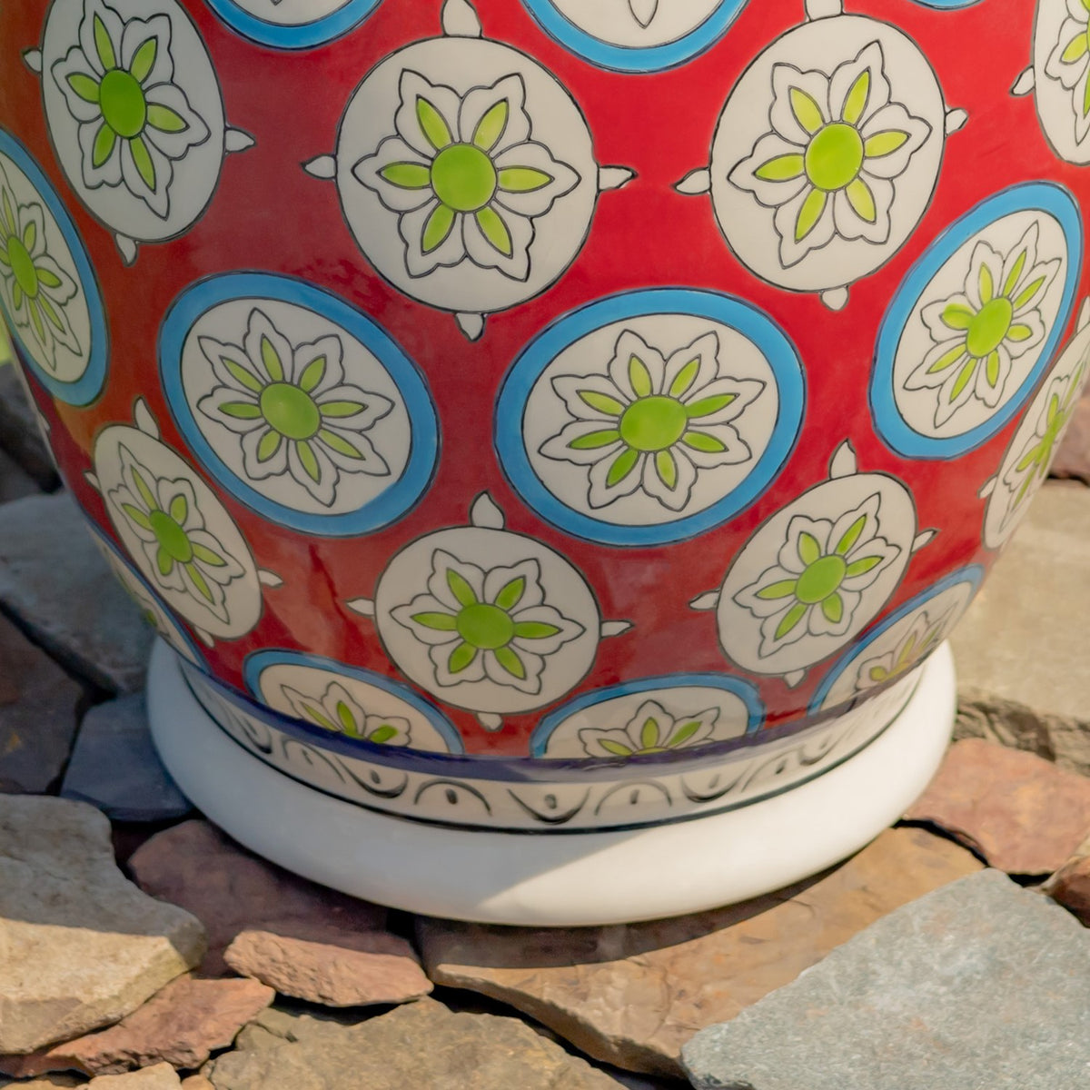 Lower portion of the patterned red ceramic stool, showing its white decorative base on a stone surface.