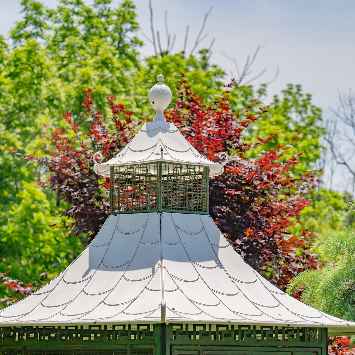 Pagoda-shaped roof with curled eaves and a finial, framed by leafy garden trees.