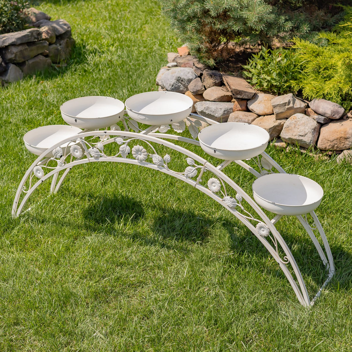 White arched metal plant stand with five empty bowls, shown on grass from above.