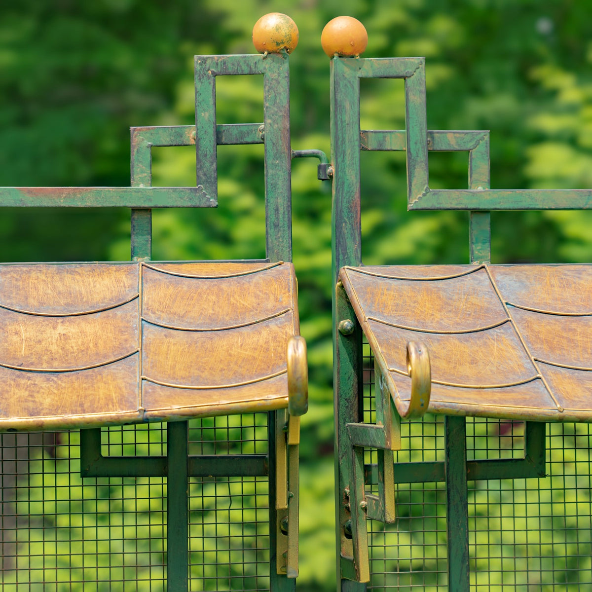 Close view of the gate's meeting panels, latch, gold-toned roof panels, and round finials.