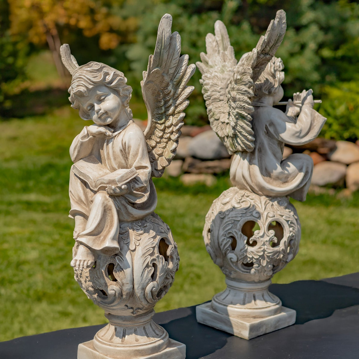 Two antique grey cherub statues viewed from the side and back outdoors