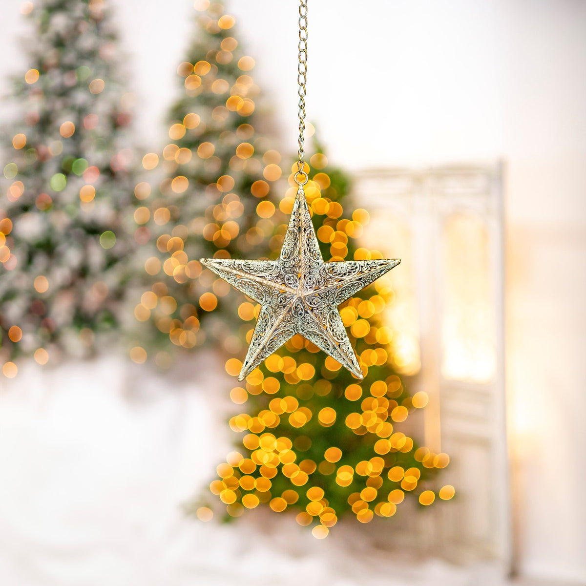 A smaller view of the patterned star ornament suspended from a chain against blurred holiday lights.
