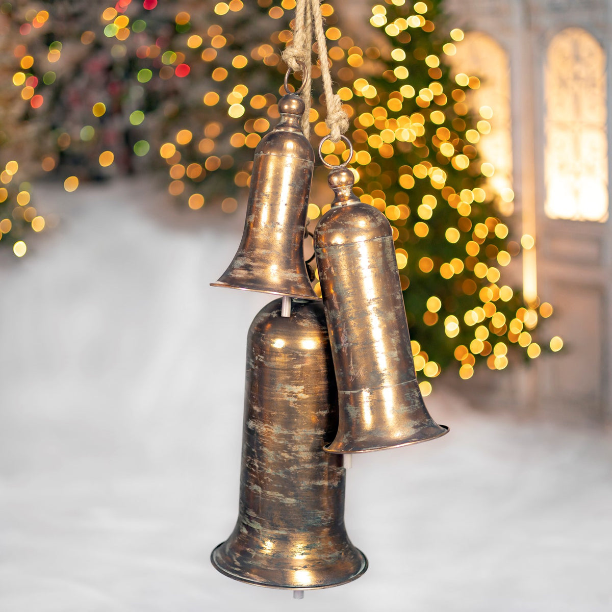 Three hanging bells with rounded tops and varied shapes shown against a softly lit holiday backdrop.