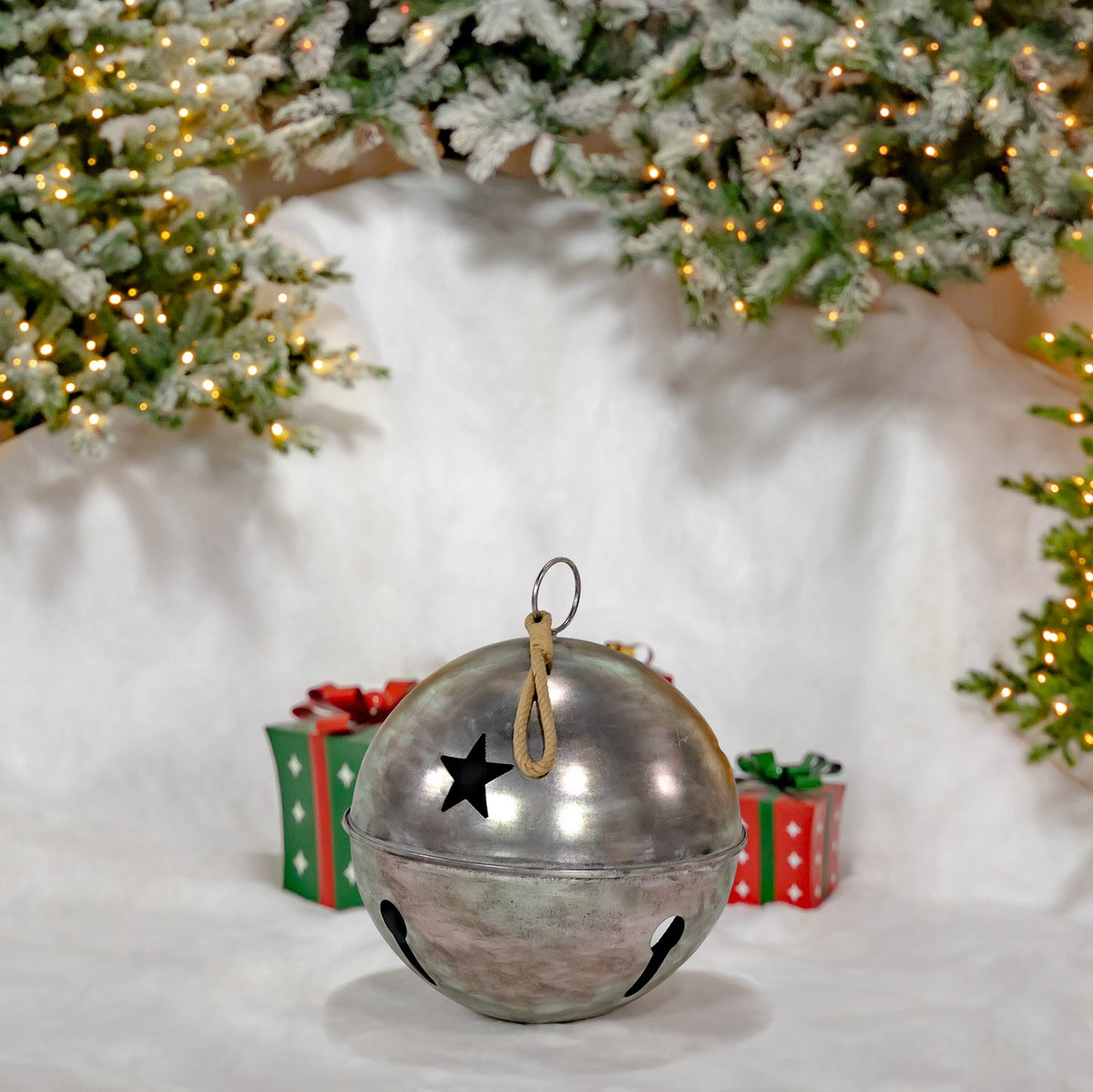 Smaller silver sleigh bell with a star cutout and hanging loop, shown against a snowy holiday scene.