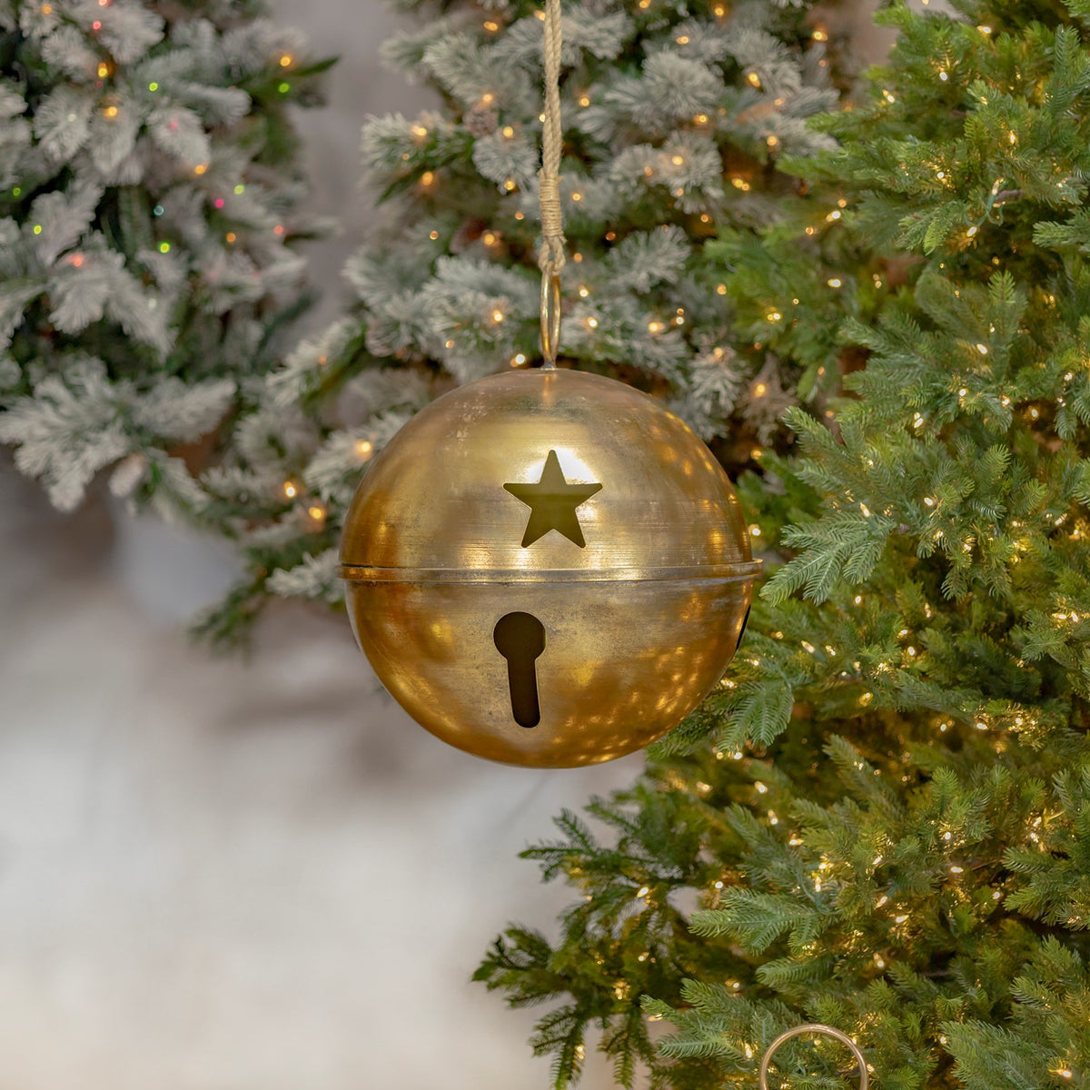Antique-gold bell hanging from a cord in front of a decorated evergreen tree, showing a star cutout.