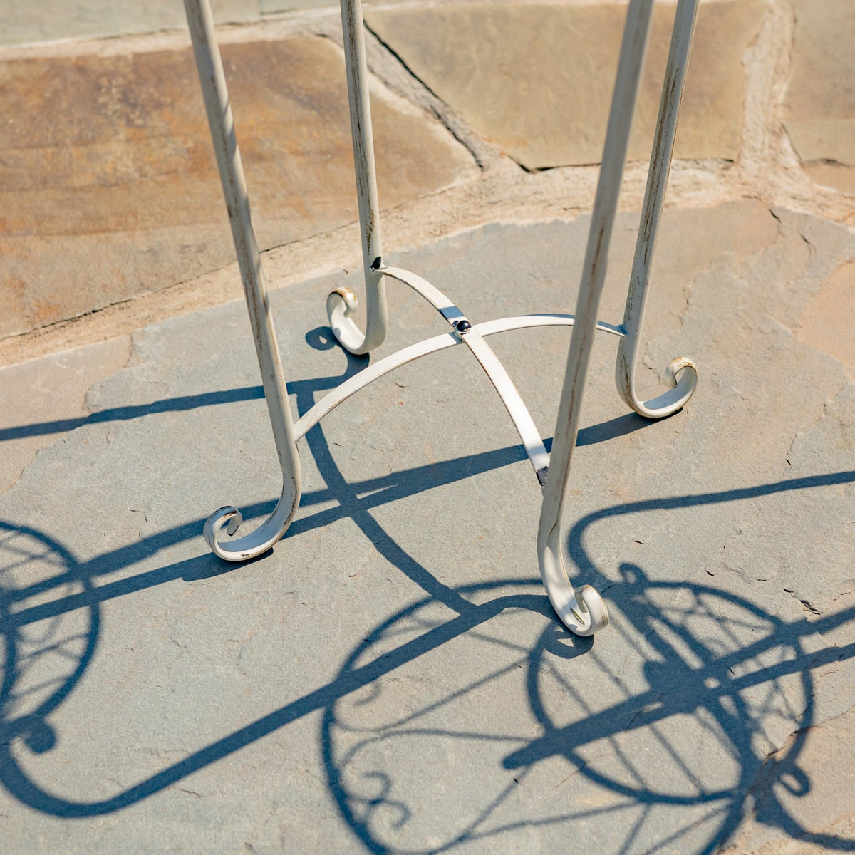 Close view of the plant stand’s slender metal legs ending in curled feet on a stone patio.