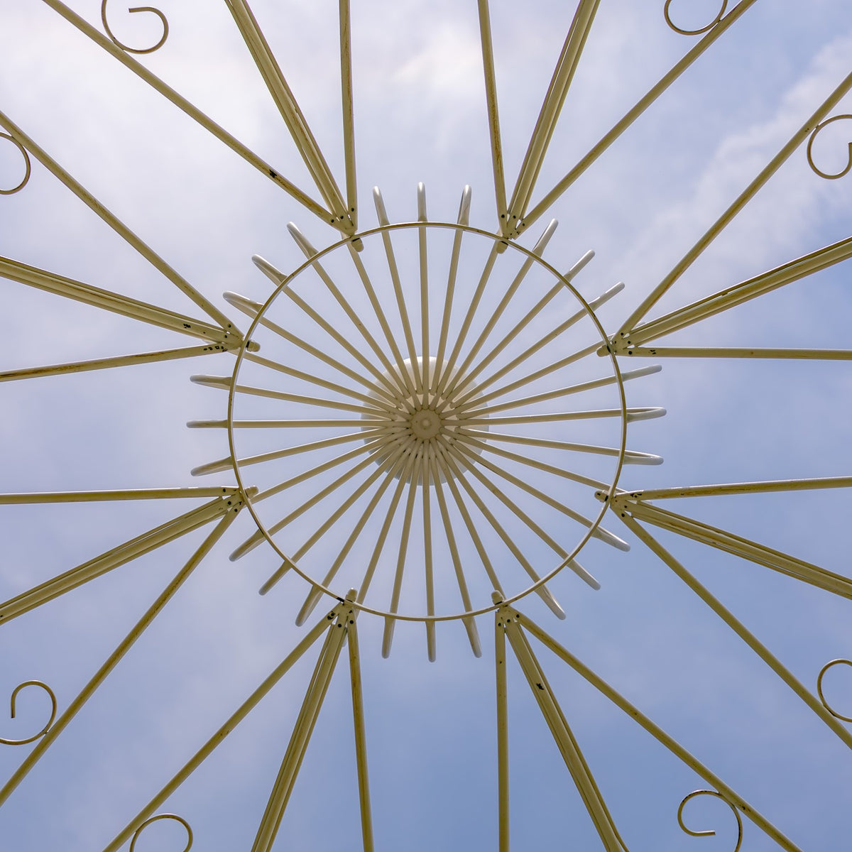 Looking up at the gazebo roof’s circular center and radiating iron spokes against the sky.