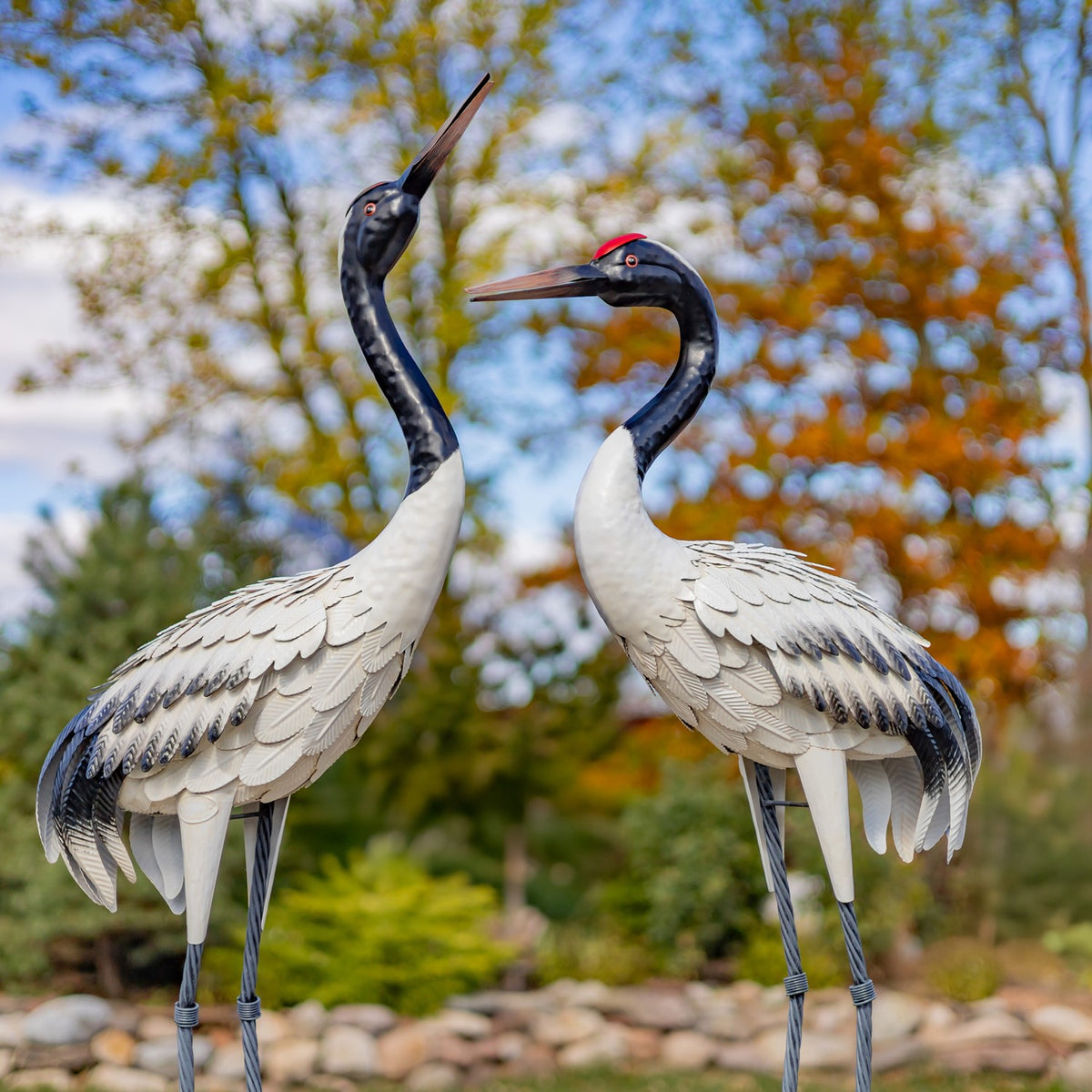 Pair of crane garden figurines shown from the front against autumn trees