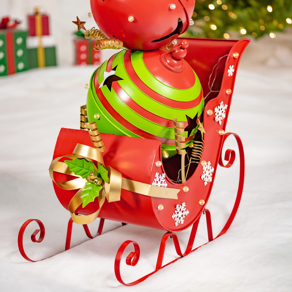 Red Christmas sleigh with curled runners, snowflake decorations, and a red-and-green jingle-bell figure.