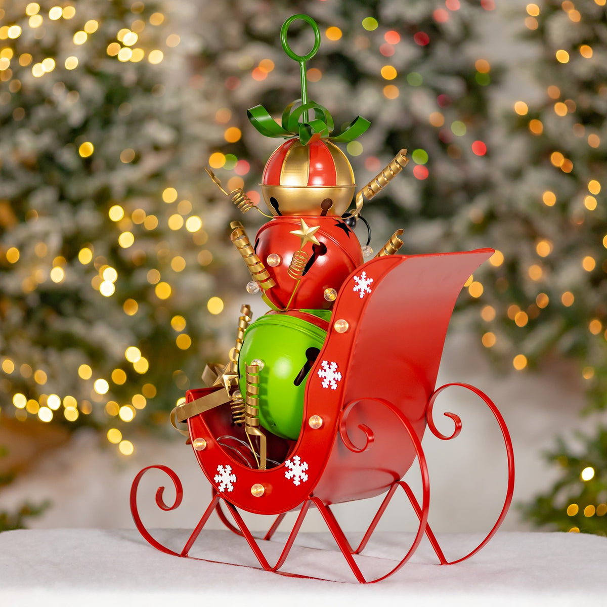 Red iron Christmas sleigh with curled runners, white snowflake accents, and colorful jingle bell decorations.