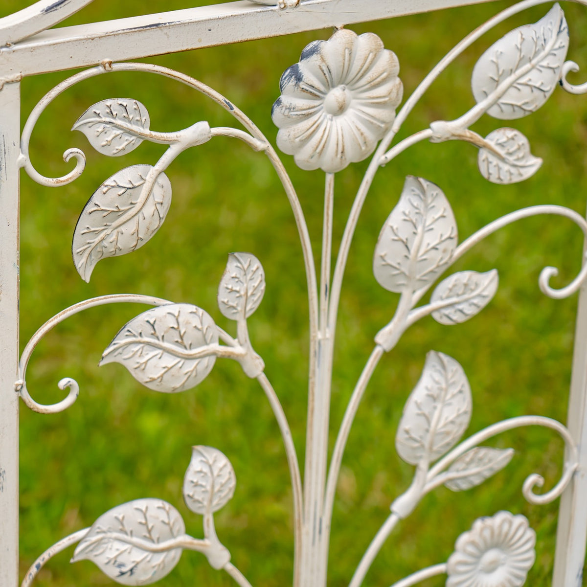 Close-up of raised metal flowers and veined leaves against curved garden gate bars.