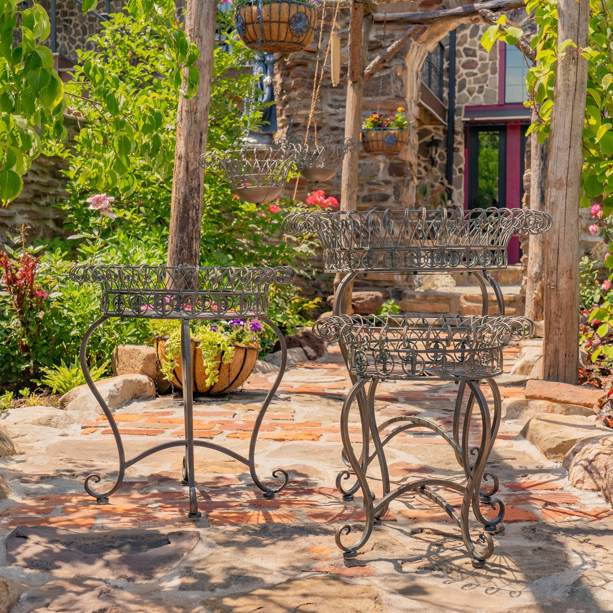 Three ornate wire plant stands of different heights displayed on a stone garden patio.