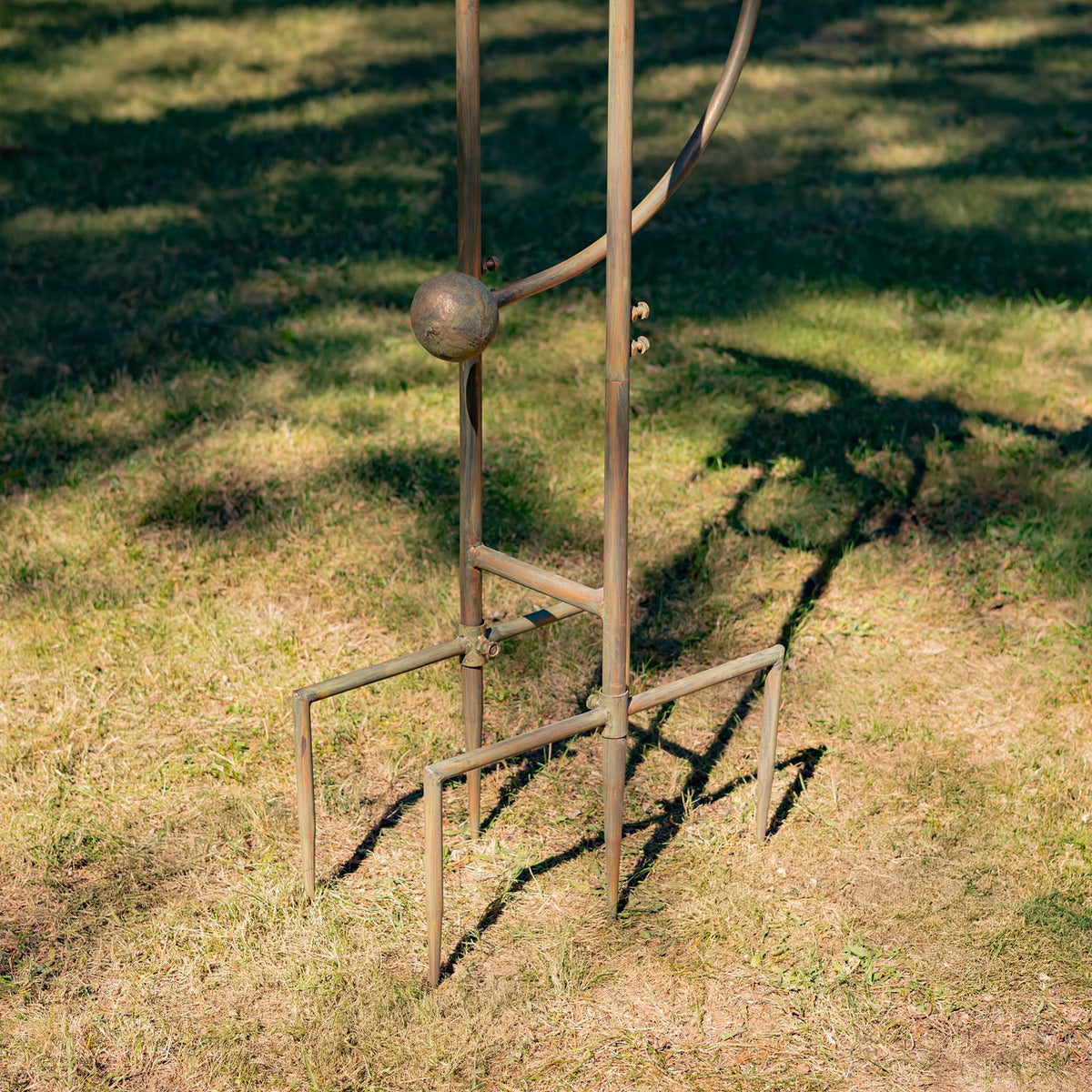 Lower iron stake and rectangular support frame standing in grass, with part of the curved rod visible.