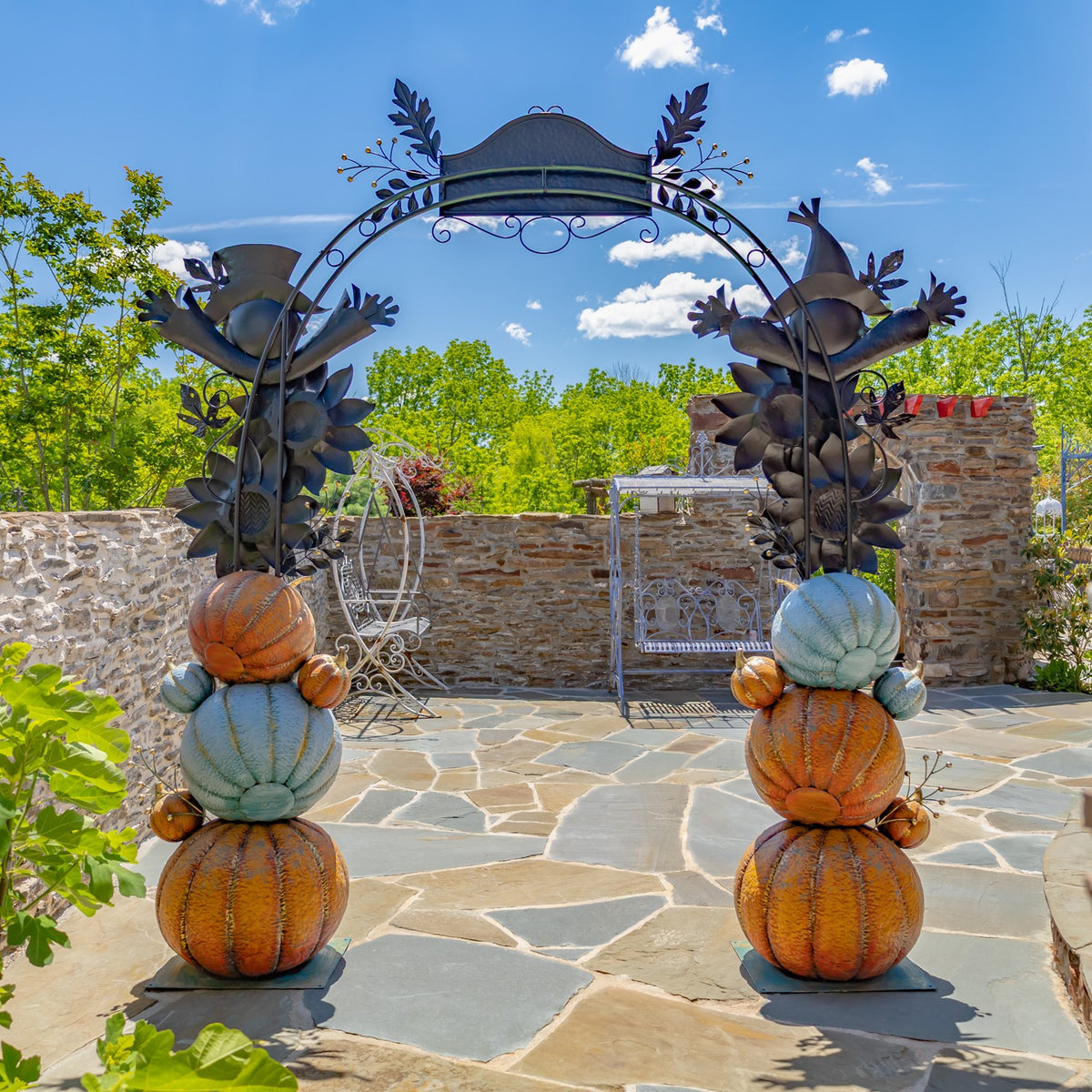 Decorative arch with sunflower accents and stacked orange and blue pumpkins framing a stone patio.