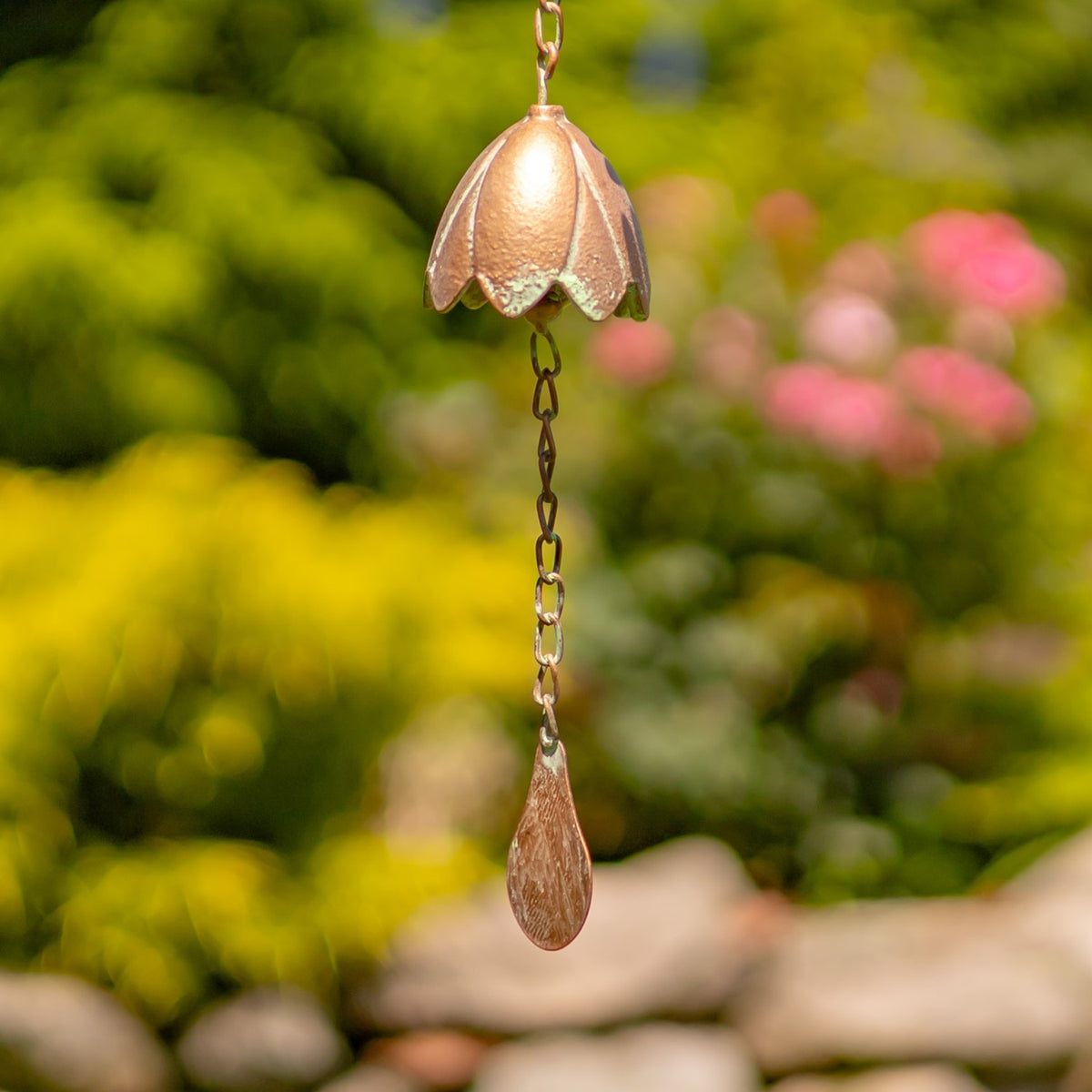 A copper-colored lily bell hangs from a chain above a long teardrop-shaped metal pendant.