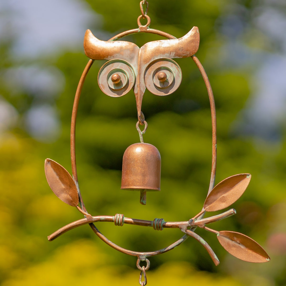 Close view of the owl-shaped rain chain ornament, showing its curled eyes, central bell and metal leaves.