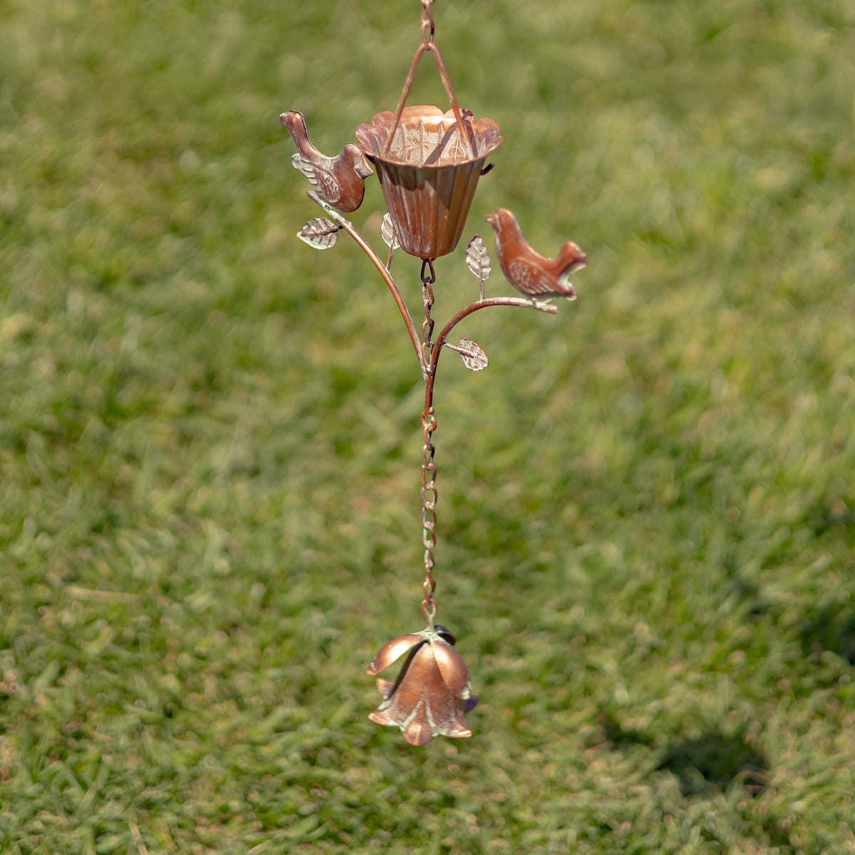 Hanging rain chain with bird and flower details, ending in a bell-shaped metal ornament.