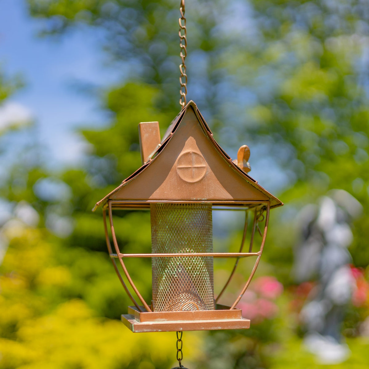 Front view of a hanging pagoda-style bird feeder, showing its peaked roof, central mesh tube and chain.