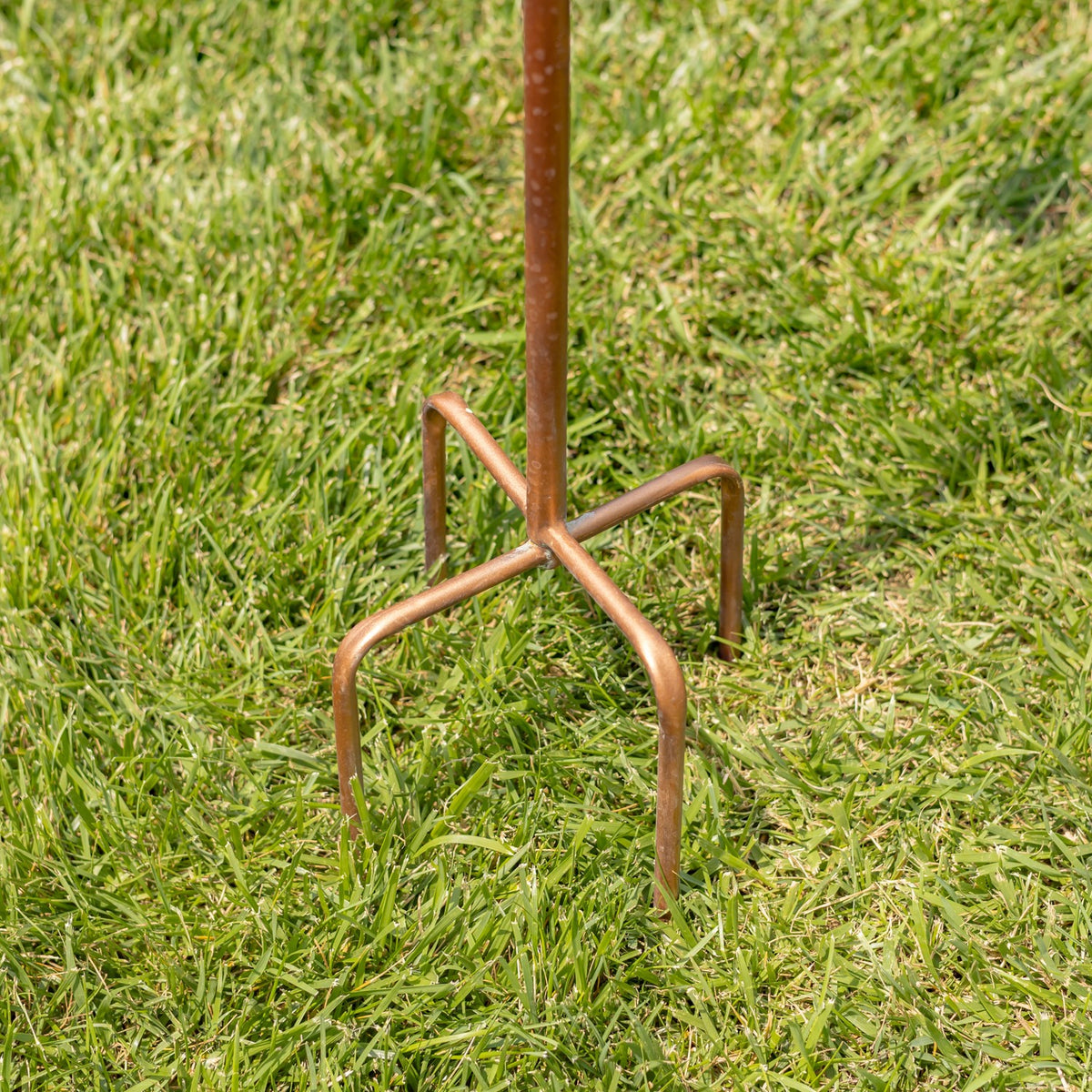 Rust-colored metal garden stake ends in four curved legs set into the grass.