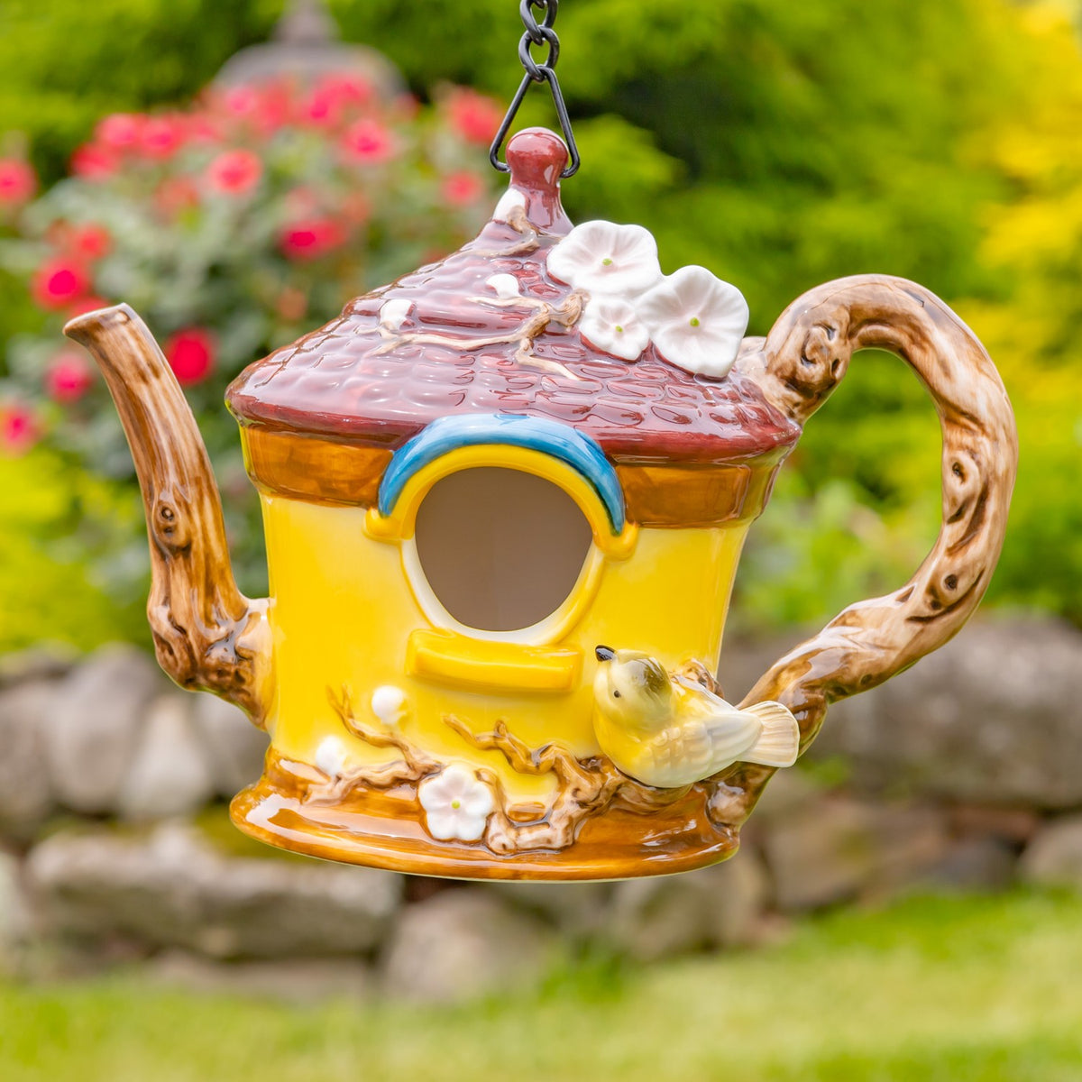 Yellow teapot birdhouse with a brown textured lid, curved handle, white flowers, and a small bird.