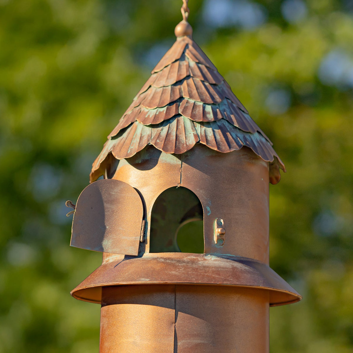 Close view of the feeder's arched opening with its small metal door swung open beneath a layered roof.